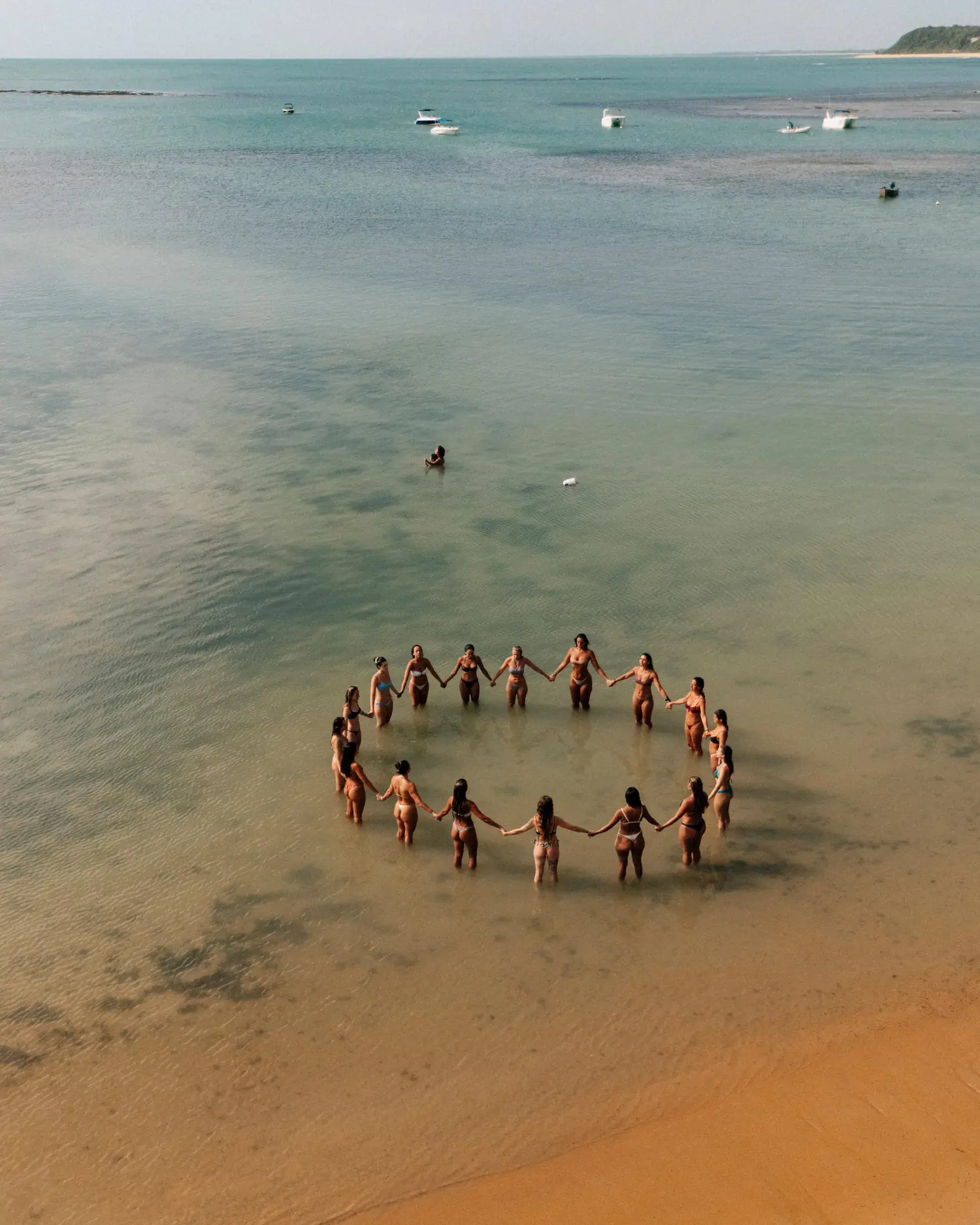 Vista aérea de un círculo de mujeres tomadas de las manos, de pie en el agua poco profunda del mar, en un retiro anterior en Brasil.
